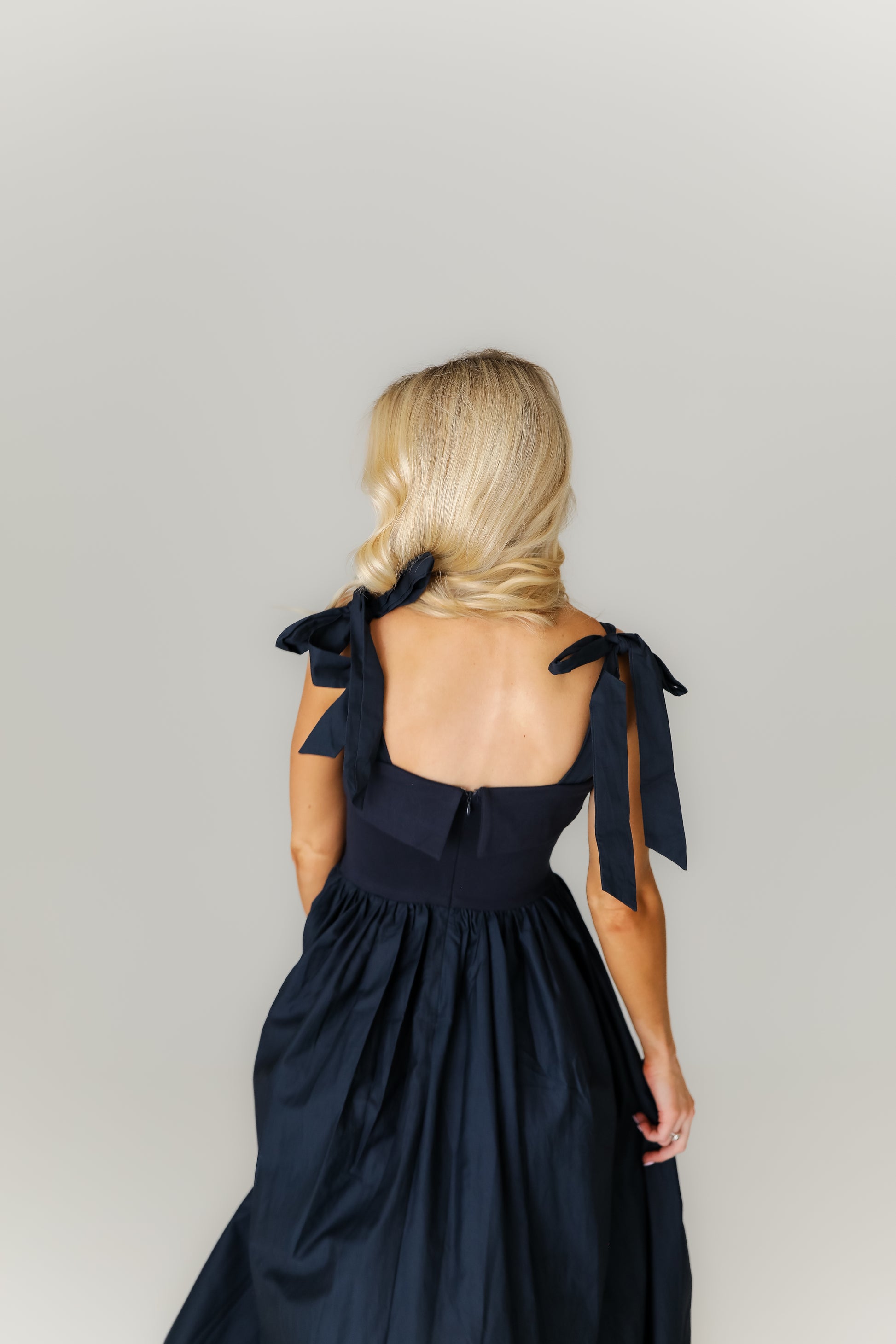 Woman wearing a black dress with bow straps against a plain background