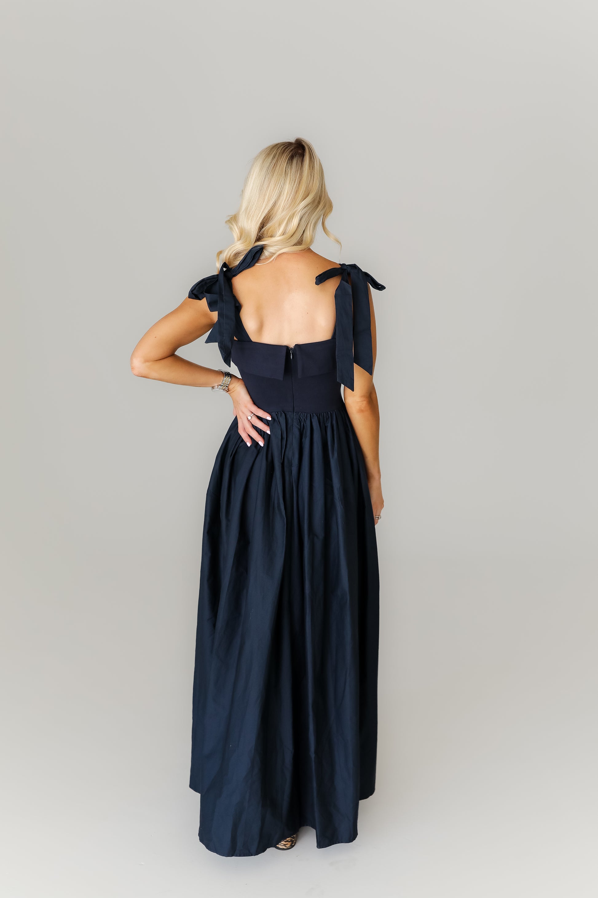 Woman wearing a navy blue dress with bow straps on a gray background