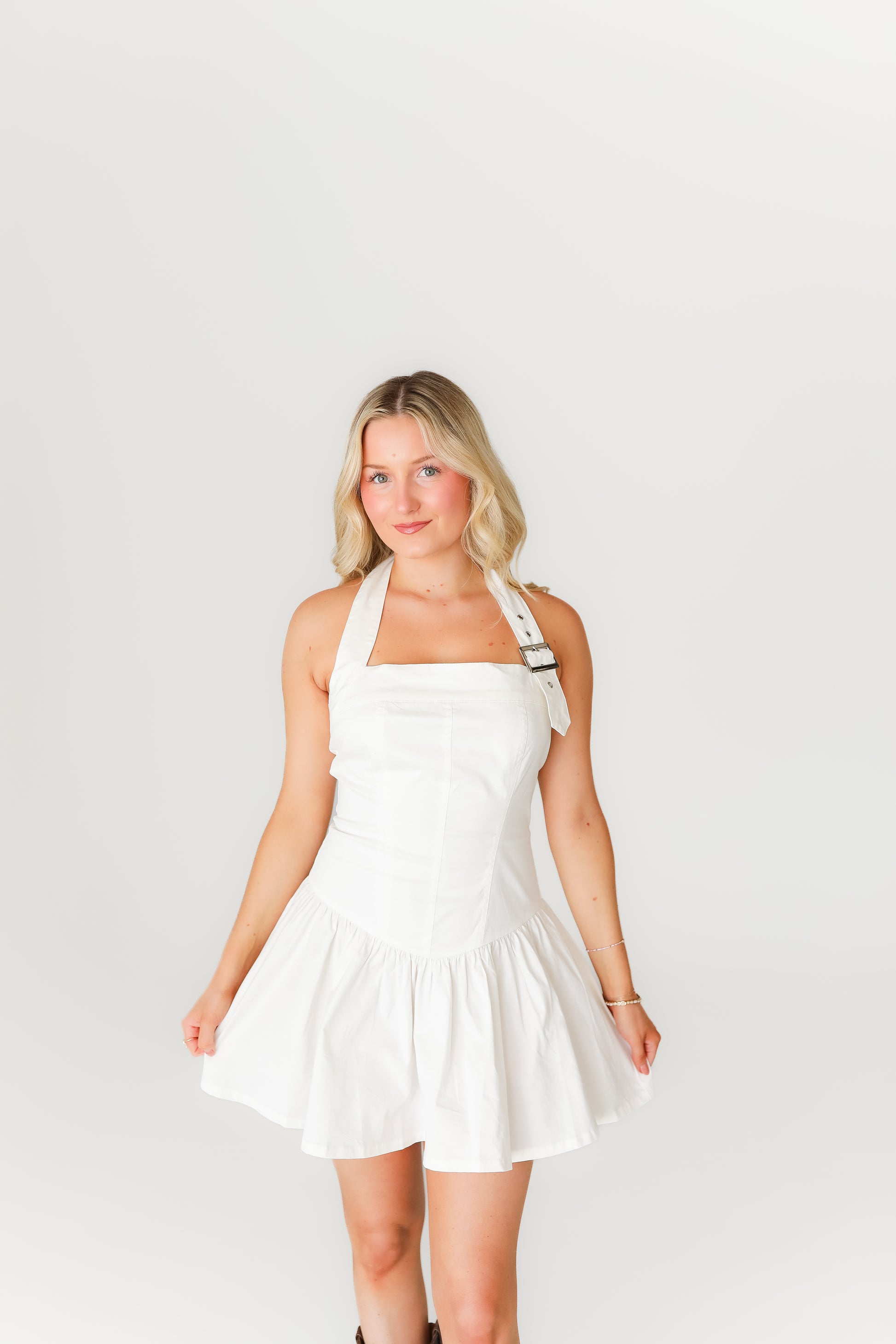 Woman wearing a white dress and brown boots on a plain background