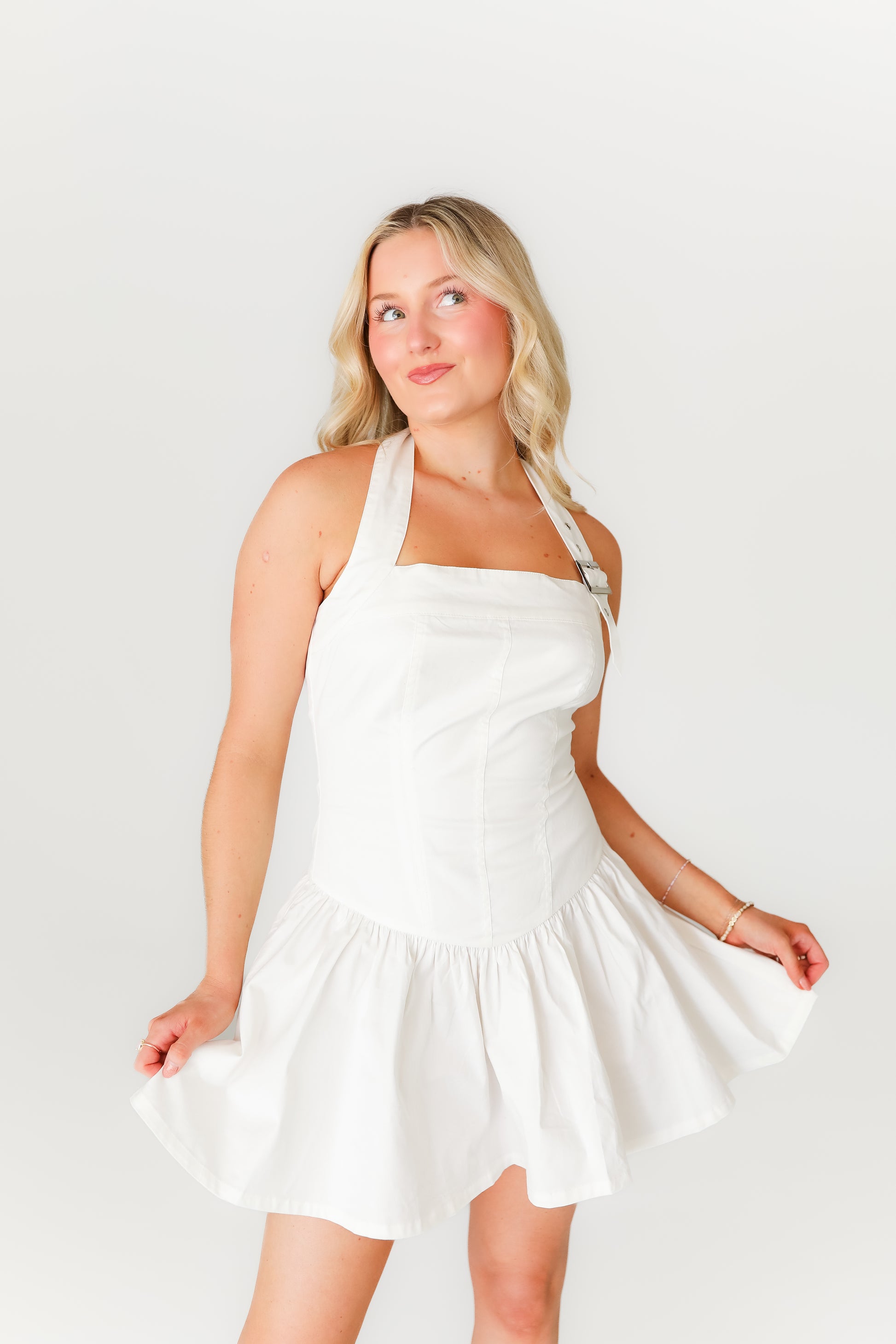 Woman wearing a white halter neck dress against a plain background