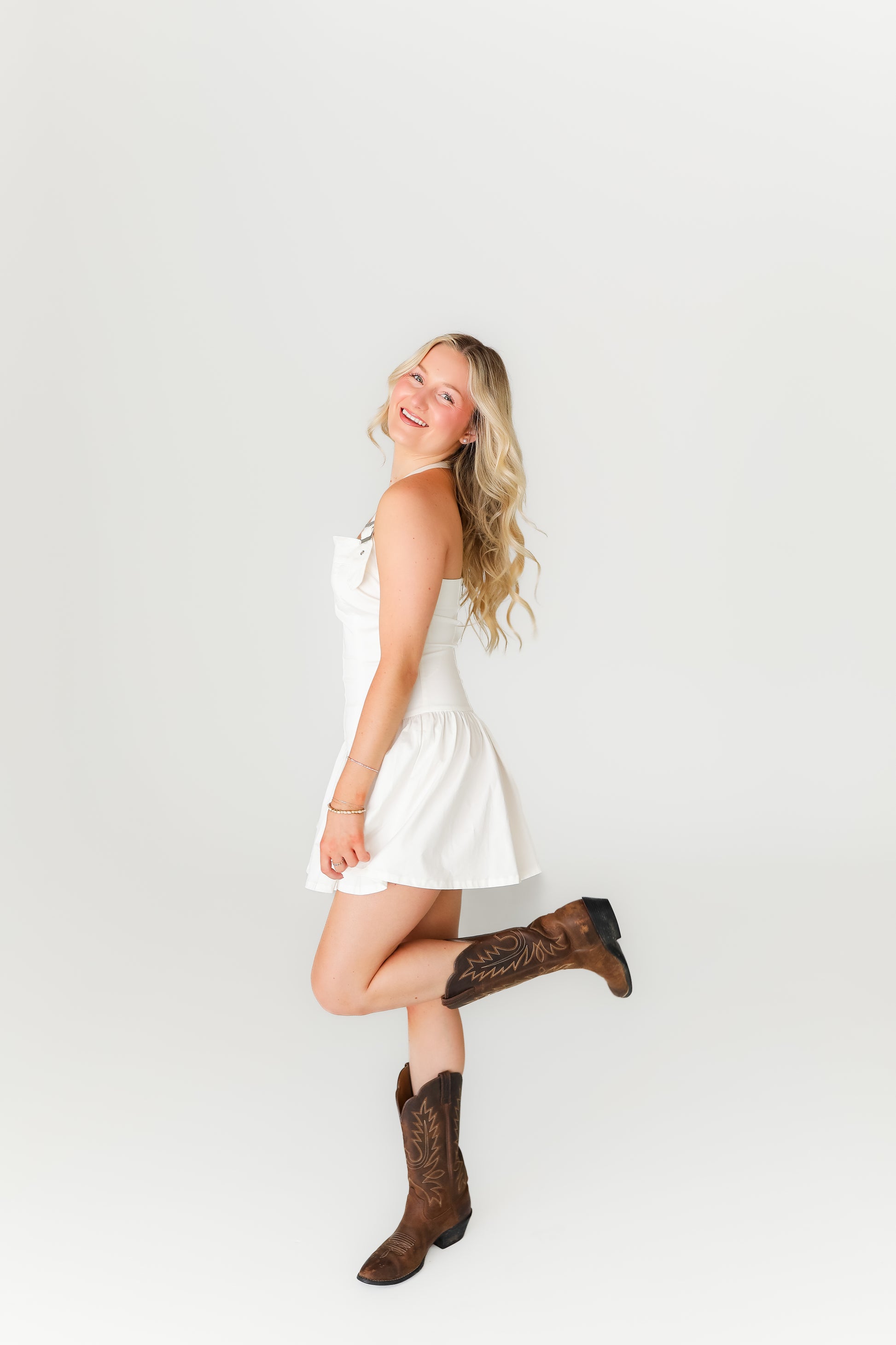 Woman in a white dress and brown boots posing against a plain background