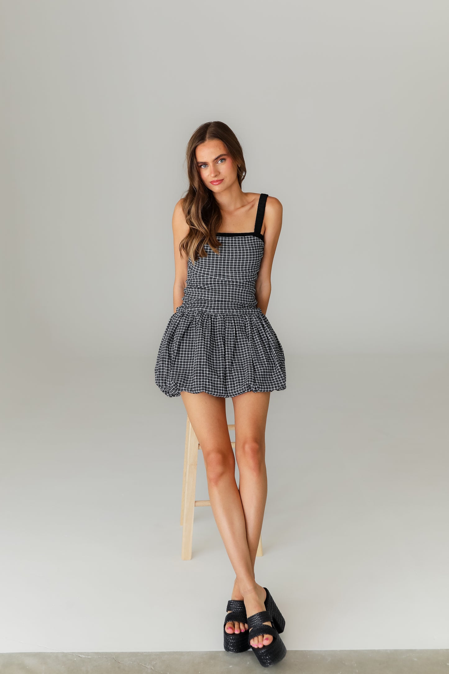 Woman wearing a black and white checkered dress standing on a stool against a plain background