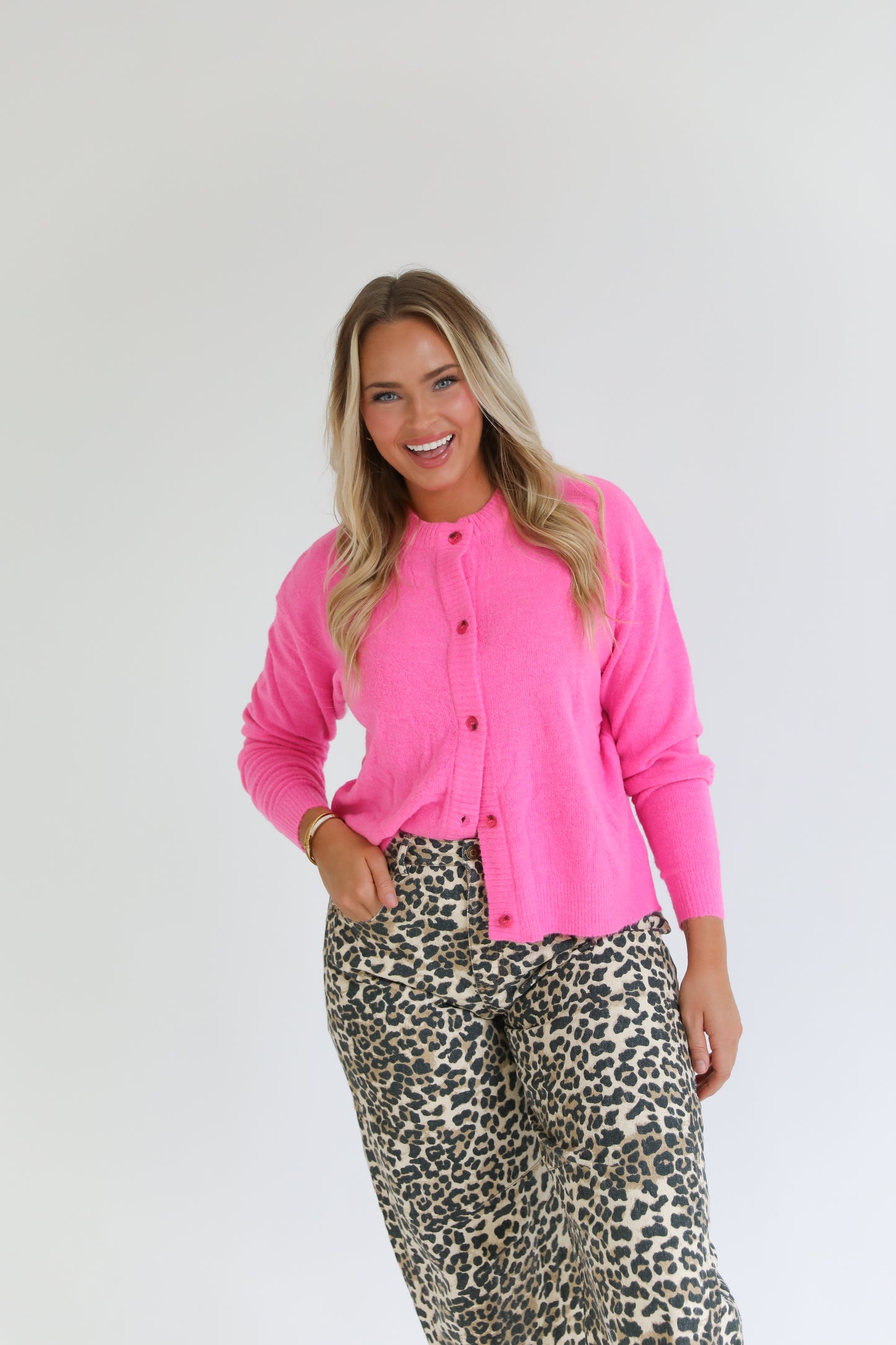 Woman wearing a bright pink cardigan and leopard print pants on a white background